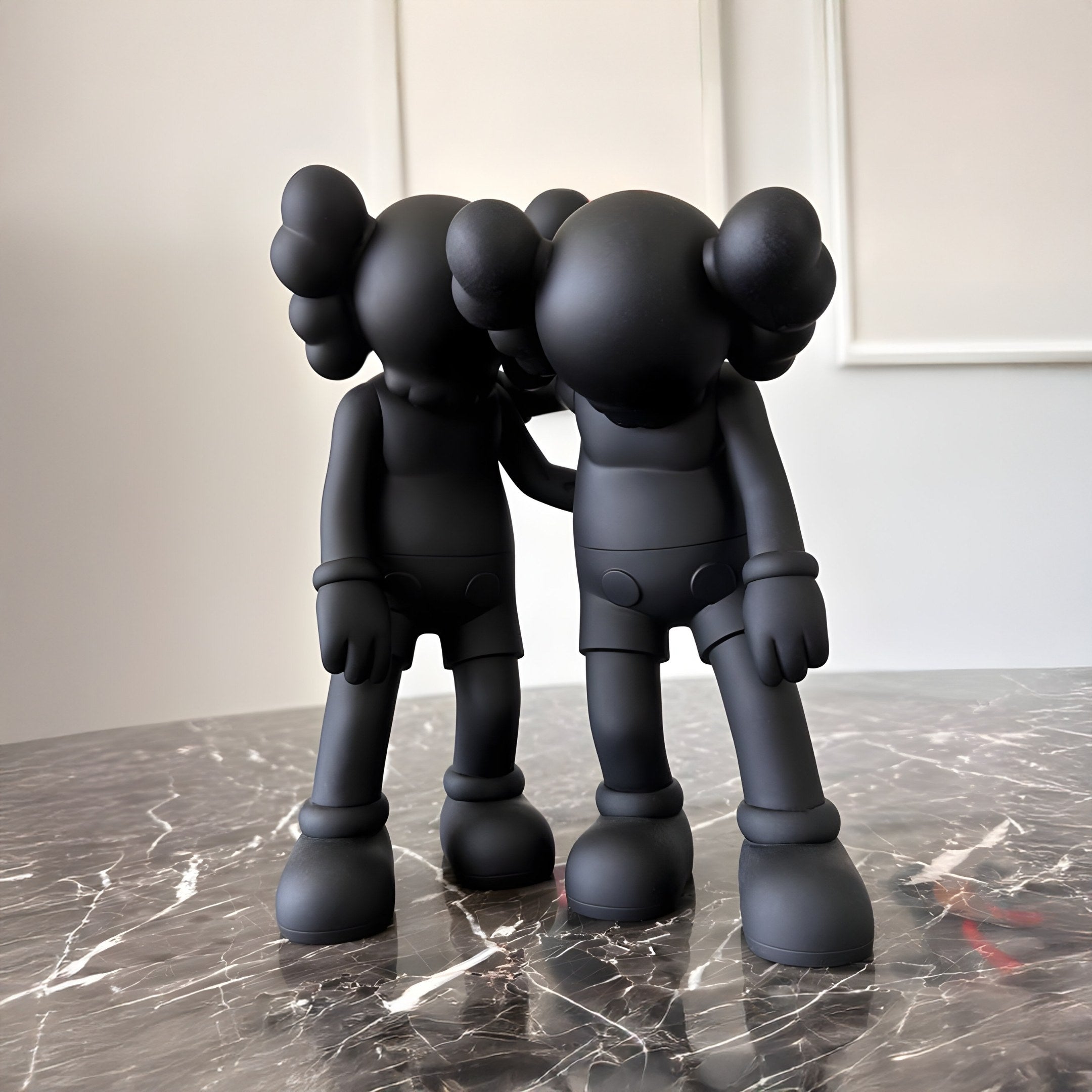 Two black, cartoon-like figures with rounded heads and oversized ears stand side by side on a marbled surface. Crafted as a resin sculpture, these characters embody the essence of a Friendship Figure, poised as if offering comfort or support to each other.