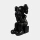 The Midnight Black Iconify Melancholy Sitting Figure by Giant Sculptures features a resin character with a head of round shapes, sitting on a block with face in hands and large rounded feet, set against a plain light grey backdrop.