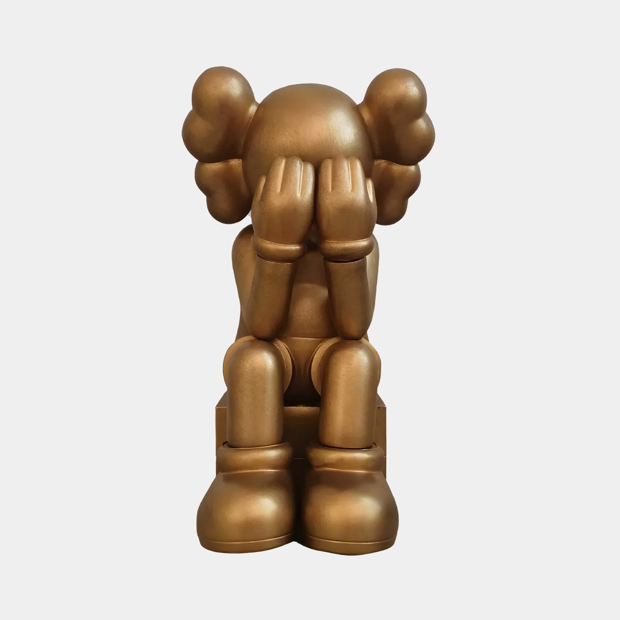 The Antique Brushed Gold Iconify Melancholy Sitting Figure by Giant Sculptures is a 28cm bronze-colored sculpture featuring a cartoonish sitting figure with hands over its face, distinct round ears, and large shoes.