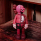 The Blush Ruby Iconify Anatomy Figure by Giant Sculptures is a 28cm contemporary piece featuring a stylized, pink and ruby red cartoonish figure. Bisected, it reveals internal organs on one side while the other displays a smooth outer skin, all set on a wooden surface.