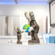 The Hazelnut Brown Iconify Atlas Figure by Giant Sculptures depicts two cartoon-like figures holding a globe, symbolizing an adult and child dynamic. Crafted from high-quality resin, it stands on a white surface with a blurred room backdrop, creating an inviting atmosphere.