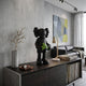 Midnight Black Iconify Dollars Figure, 30cm, holding green cash on a dark sideboard beside a marble vase and abstract wall art.