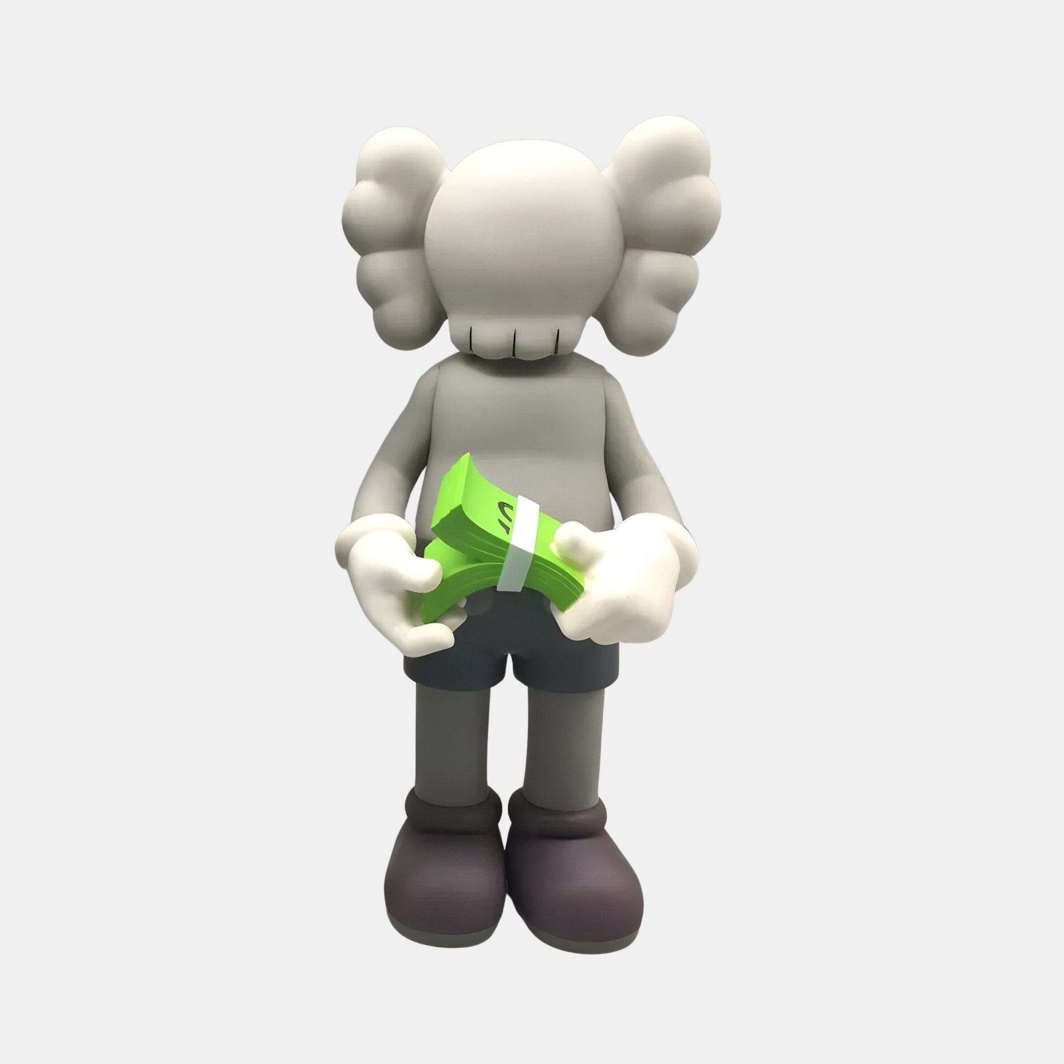 A figure from Giant Sculptures, the 30cm Soft Grey Iconify Dollars Figure, resembles a cartoonish character with a rounded head and cloud-like ears, holding green bills. This resin sculpture is an artistic statement on materialism, with simple eyes and dark shorts against a neutral backdrop.