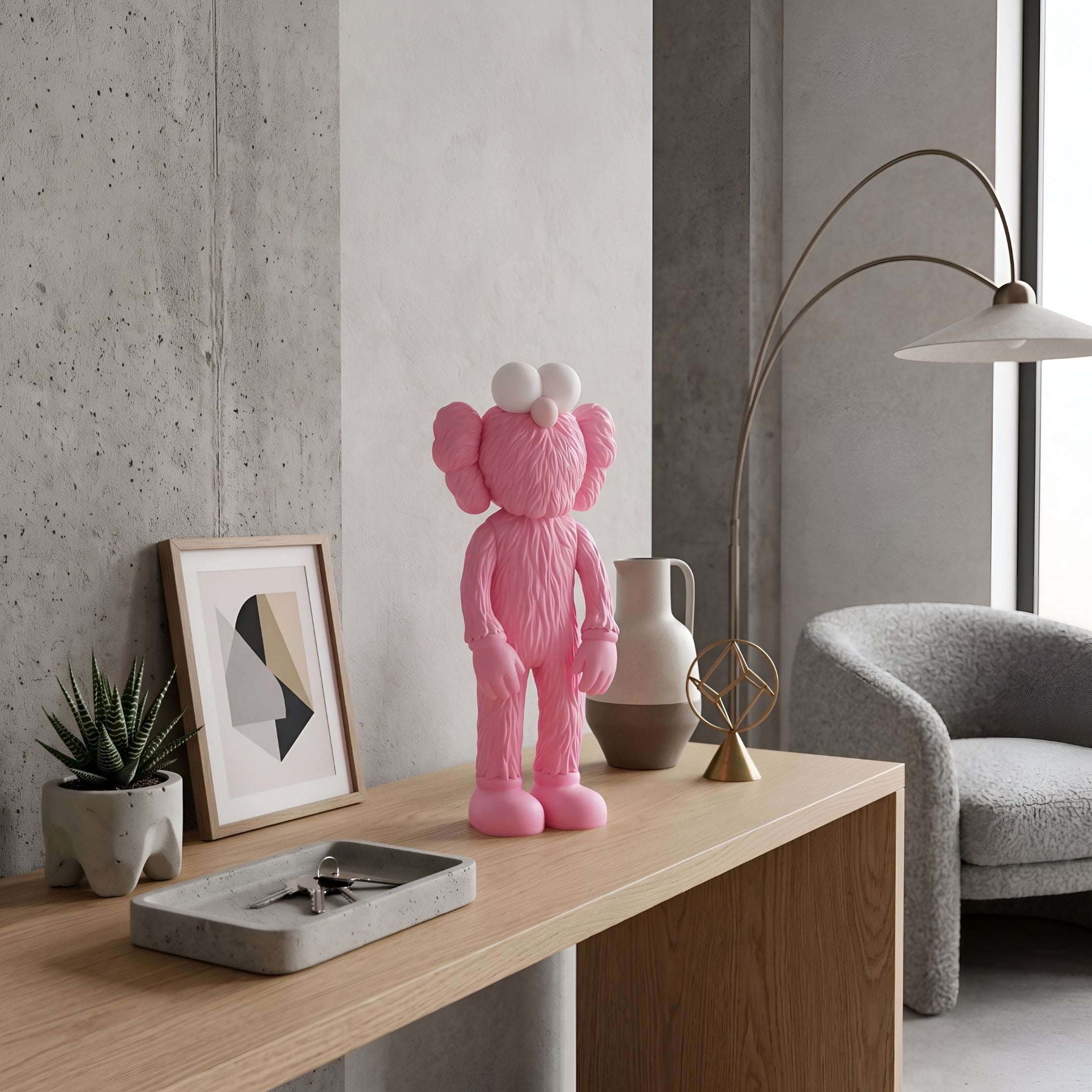 Petal Pink Iconify Furry Figure, 30cm, on a wooden desk beside a ceramic vase, framed art print, and plant in a modern living room.