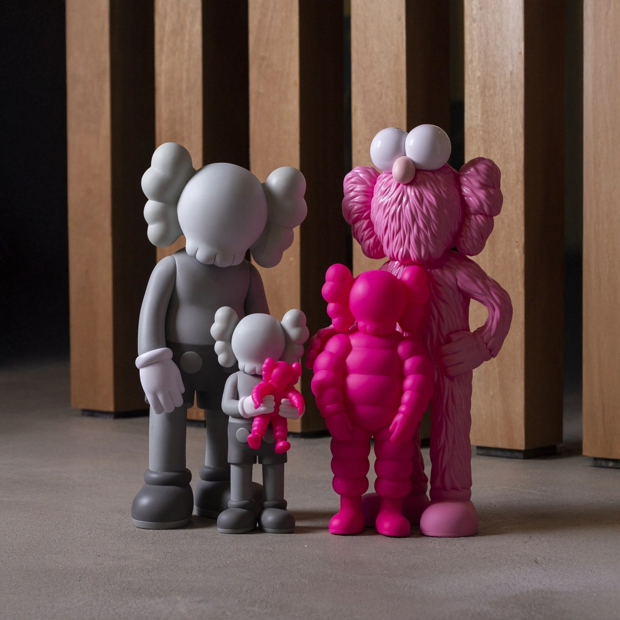 The Iconify III All-Together Figure by Giant Sculptures features four colorful, cartoonish resin figurines with gray balloon hands and pink furry textures. These figures exude charm and unity, making them ideal for contemporary interiors as they pose on a concrete floor before a wooden structure.