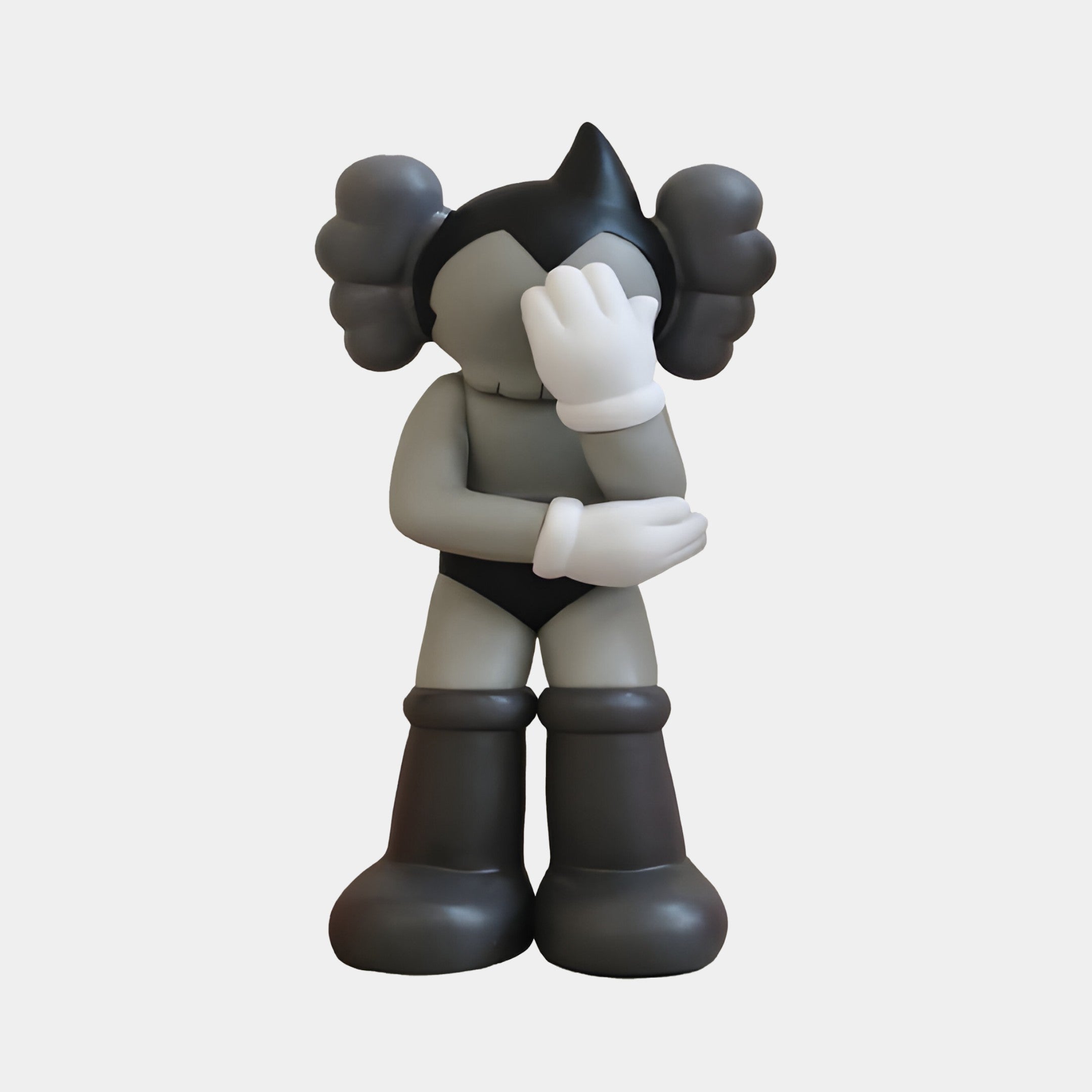 The Slate Grey Iconify Cosmic Boy Figure by Giant Sculptures is a 37cm resin piece featuring a cartoon-style character with gloves and large boots obscuring its face. Its design blends modern minimalism with playful, contemplative vibes and unique round ear-like features.