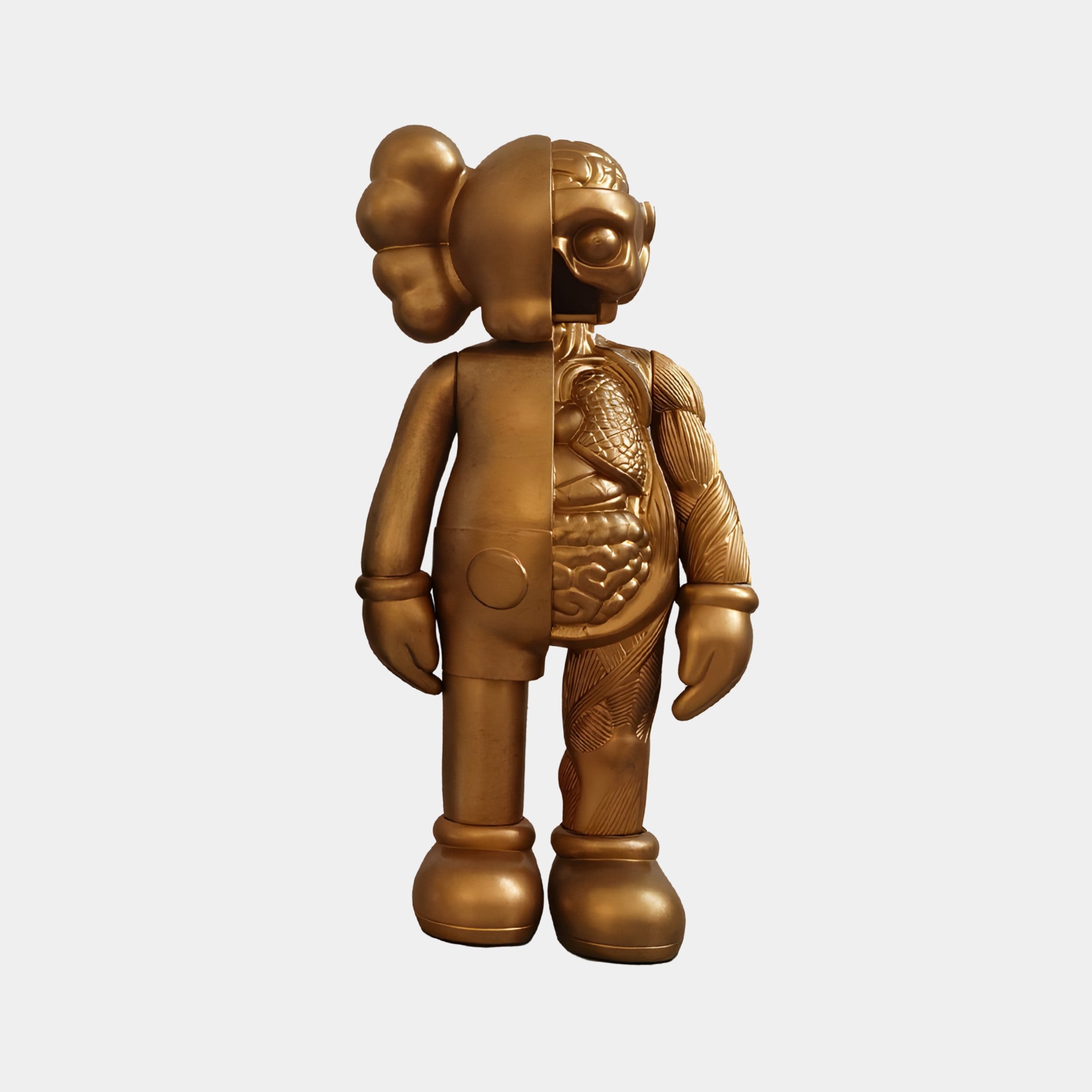 The Antique Brushed Gold Iconify Anatomy Figure by Giant Sculptures features a 37cm resin sculpture with a split design: its left side is smooth and rounded, while the right displays detailed anatomy-like textures, adorned with large gloves, boots, and a distinctive head shape.