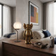 Antique Brushed Gold Iconify Standing Figure, 37cm, displayed on a wooden dresser in a bedroom beside a globe table lamp and framed abstract art.