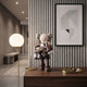 Hazelnut Brown Iconify Family Figure, 38cm, on a wood console table beside a framed abstract print, gold tray, and glowing globe floor lamp in a modern hallway.