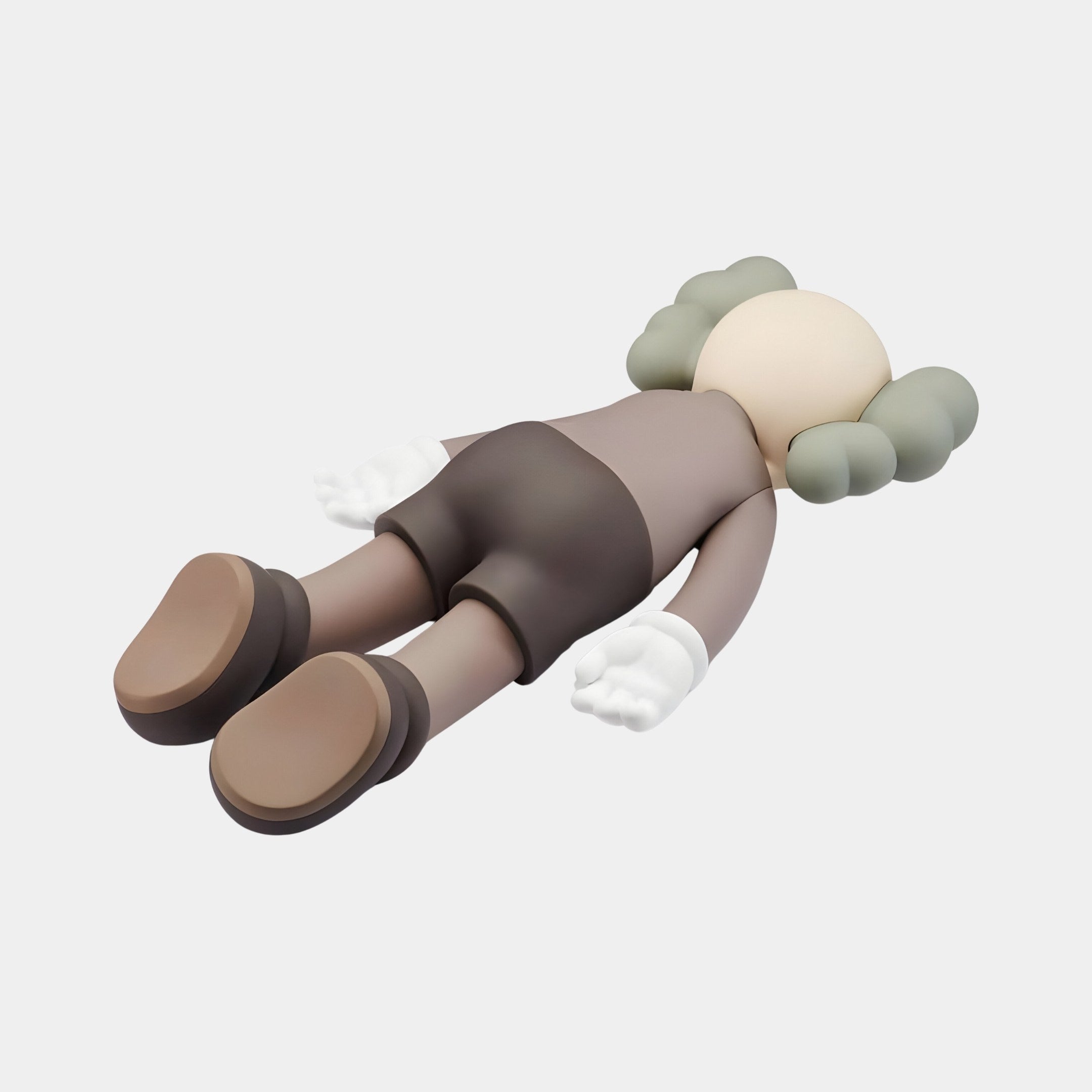 The Hazelnut Brown Iconify Flat Figure by Giant Sculptures lies flat on a white surface. With a rounded head and gray hair, beige face, white gloves, brown shorts, and matching shoes, its extended arms and legs showcase elegance in contemporary interiors. Size: 38cm.