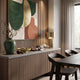 Sideboard vignette with abstract wall art, green vase, and brass table lamp, styled near a dark dining table and chairs.
