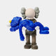 The Giant Sculptures Royal Blue Iconify Rescuing Figure (38cm) features a skull-faced cartoon figure with grey ears cradling a blue, furry character with closed eyes and a yellow nose. The exaggerated features create a striking contrast against the plain white background, embodying contemporary artistry.