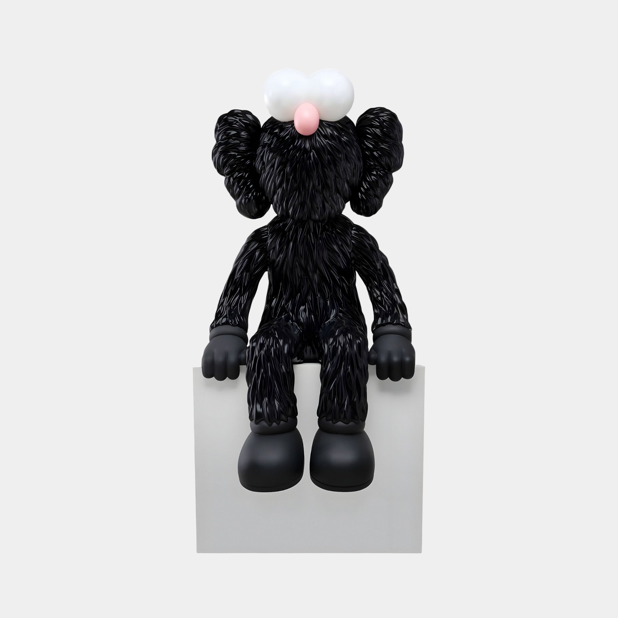 The Giant Sculptures Obsidian Black Iconify Furry Sitting Figure (40cm) features large white eyes, a pink nose, oversized black shoes, and distinctively shaped ears. Seated on a white block, it creates a modern focal point against the plain background.