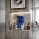 Deep Blue Iconify Furry Sitting Figure, 40cm, on a white plinth in a wall niche shelf with magazines, a potted plant, and framed art nearby.
