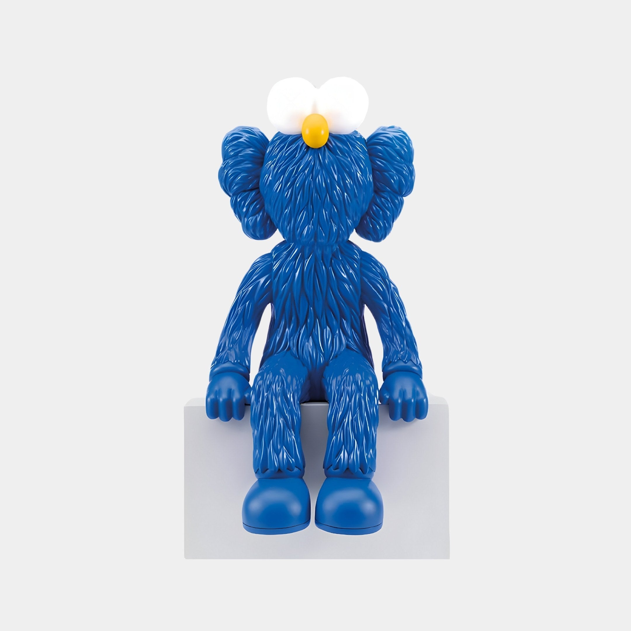 The Giant Sculptures Deep Blue Iconify Furry Sitting Figure features large ears and a round, featureless head. It sits on a white block, exuding Pop Art charm with a white flower and vivid yellow center atop its head.