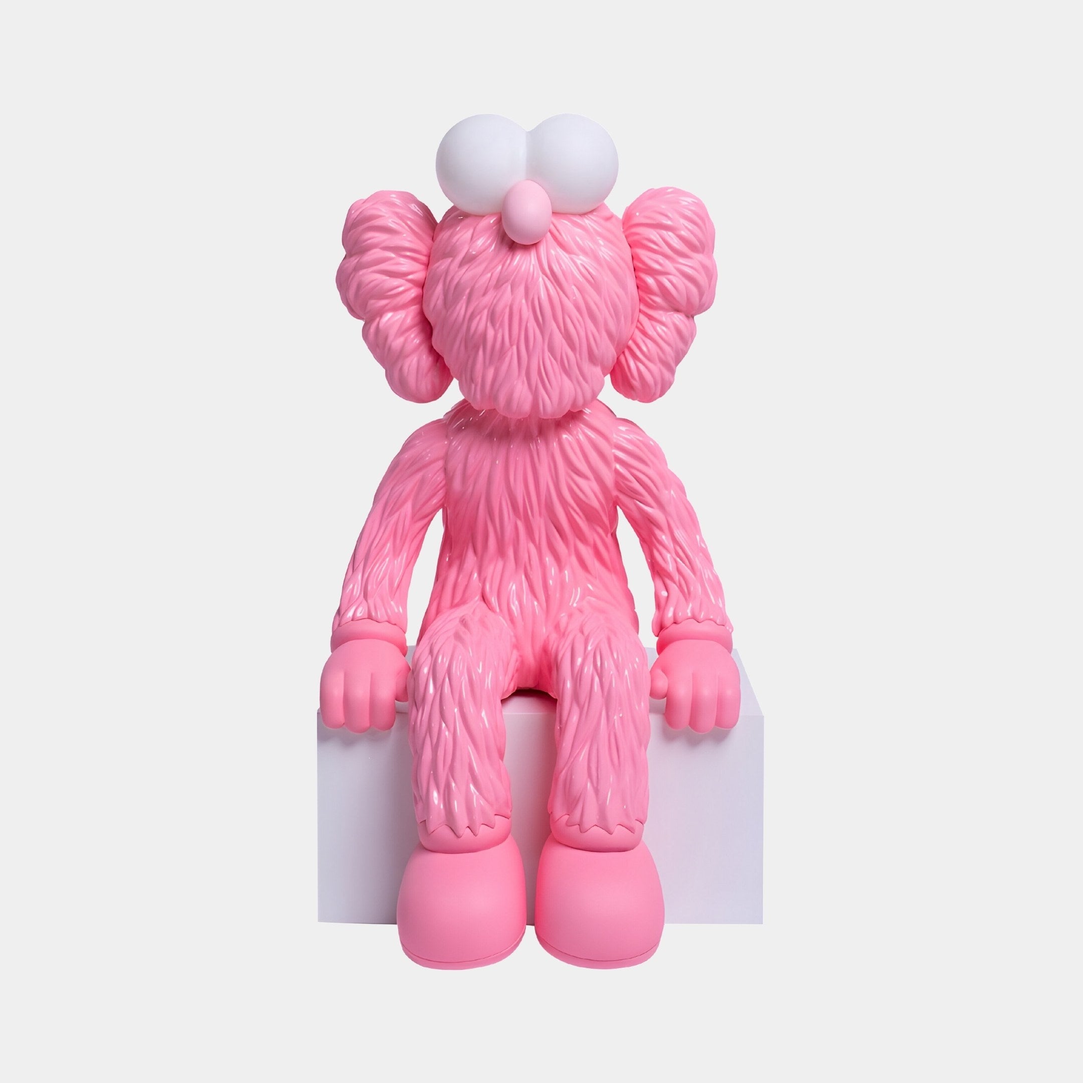 The Petal Pink Iconify Furry Sitting Figure by Giant Sculptures features a 40cm furry sitting figure with large round eyes and a bulbous nose perched on a white block. Its textured surface and oversized shoes add charm, against a plain light gray background.