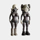 The Smoky Umber Gray Iconify Vera Dolls Figures by Giant Sculptures captivate with their smoky umber gray, bubble-shaped heads, heart chest details, distinct hair and footwear styles. At 40cm tall, they stand side by side against a plain backdrop, sparking artistic intrigue.