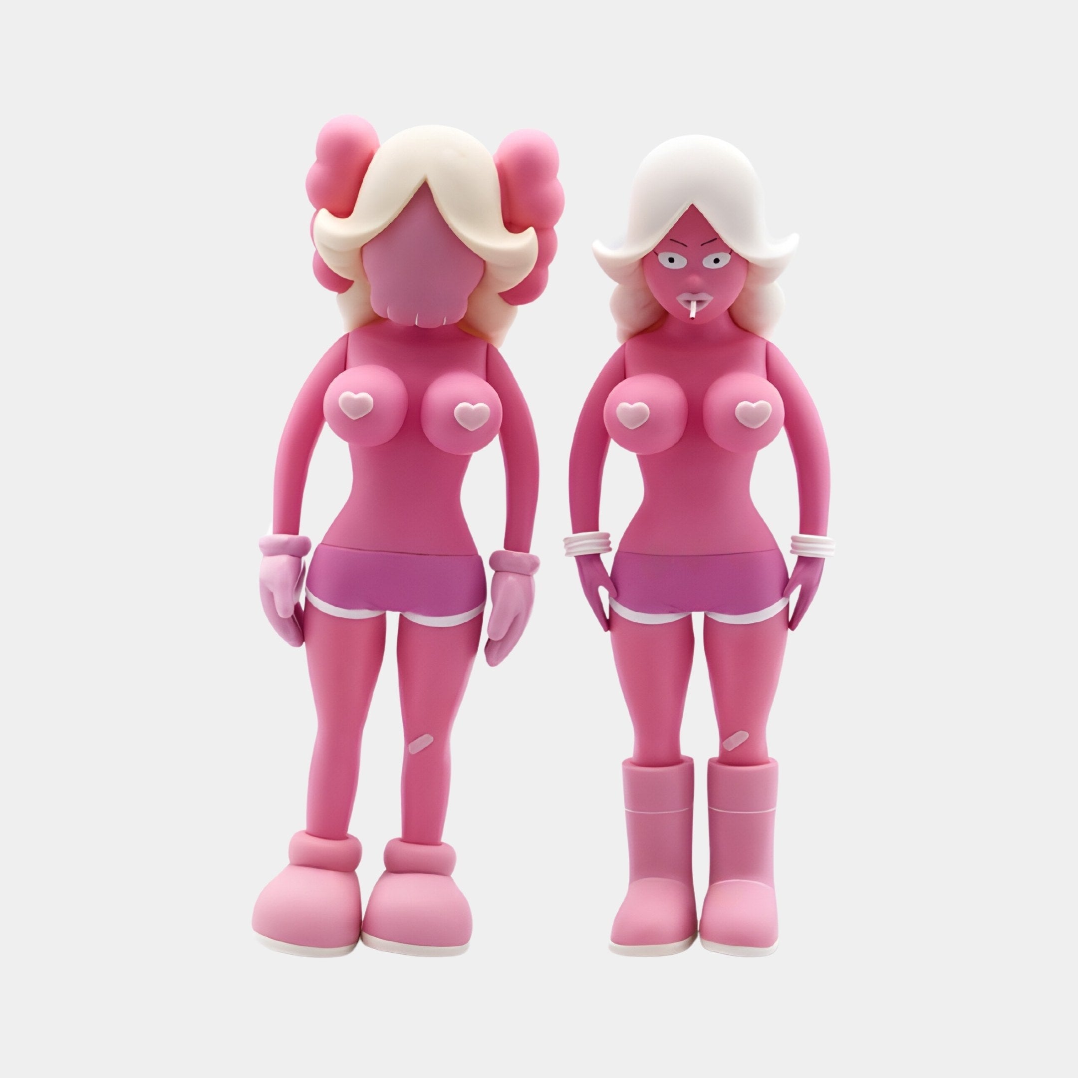 The Rosewood Blush Iconify Vera Dolls by Giant Sculptures feature two avant-garde pink figures with similar body shapes, heart-shaped chests, unique hairstyles, boots, gloves, and exaggerated features. The right one playfully adds a pacifier to its look. Each figure stands 40cm tall.