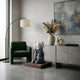 Slate Grey Iconify Melancholy Sitting Sculpture, 70cm, on a wooden plinth beside a green armchair and grey sideboard in a living room setting.