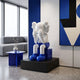 White & Blue Iconify Melancholy Sitting Sculpture, 70cm, seated figure covering face on blue block base, black plinth, in a lounge with grey sofa and blue art.