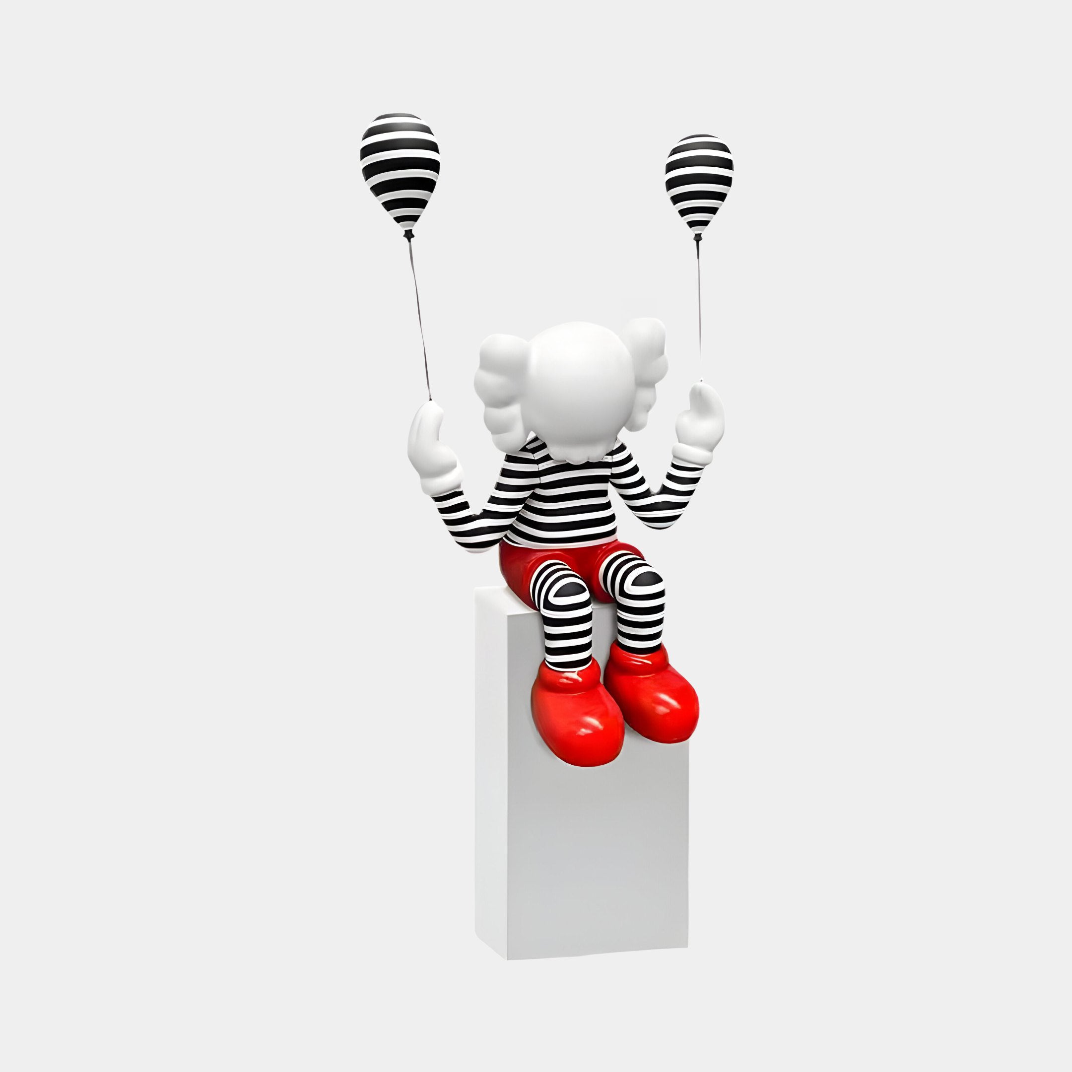 The Lustrous Red Iconify Mime Sitting Sculpture by Giant Sculptures features a whimsical figure with a white face, wearing black and white stripes, lustrous red shoes, and holding matching striped balloons.