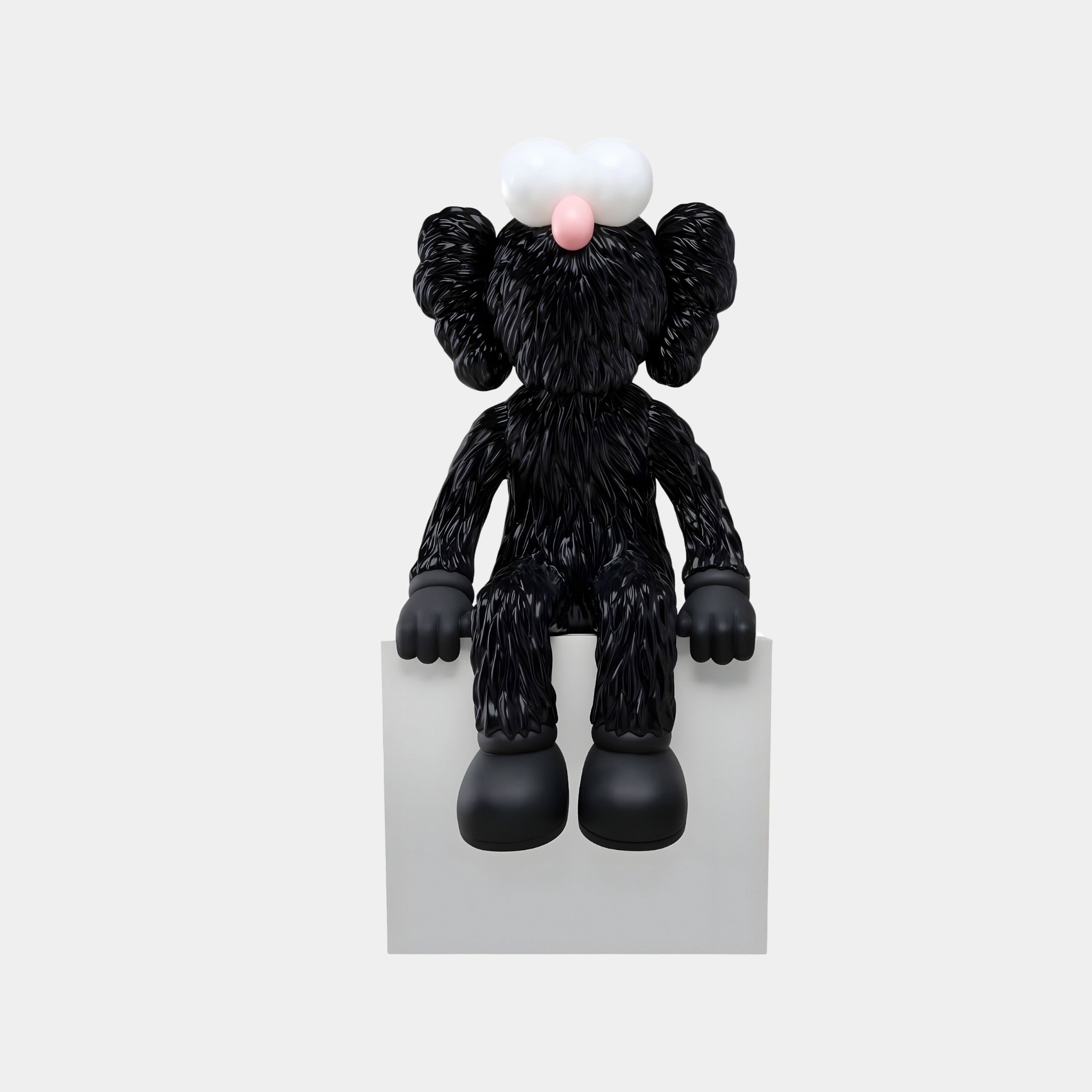 The Obsidian Black Iconify Furry Sitting Sculpture by Giant Sculptures features round ears, a pink nose, and white eyes on a white block. Its fuzzy texture and dangling legs create a charming presence in modern interiors against a gray backdrop.