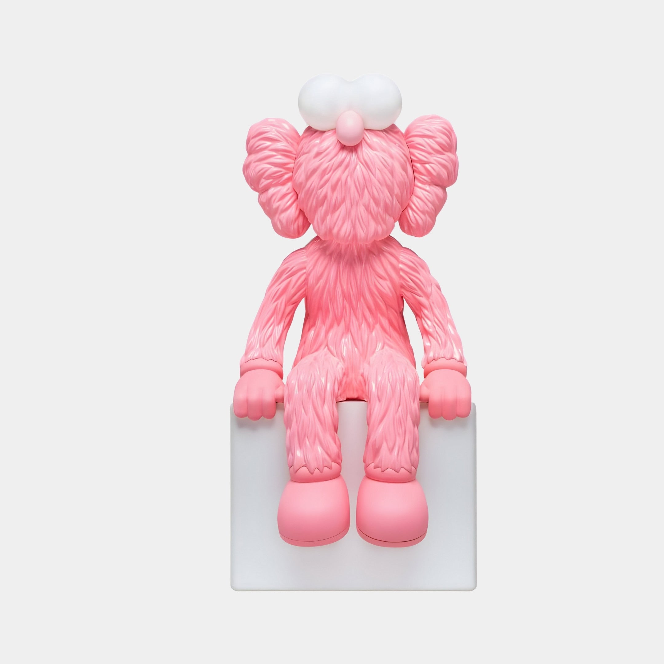 The Giant Sculptures Petal Pink Iconify Furry Sitting Sculpture (70cm) is an abstract pink figure with a fur-like texture, exaggerated ears, a round nose, and bulbous eyes. Perfect for modern interiors, it sits on a white block with limbs hanging down the sides.