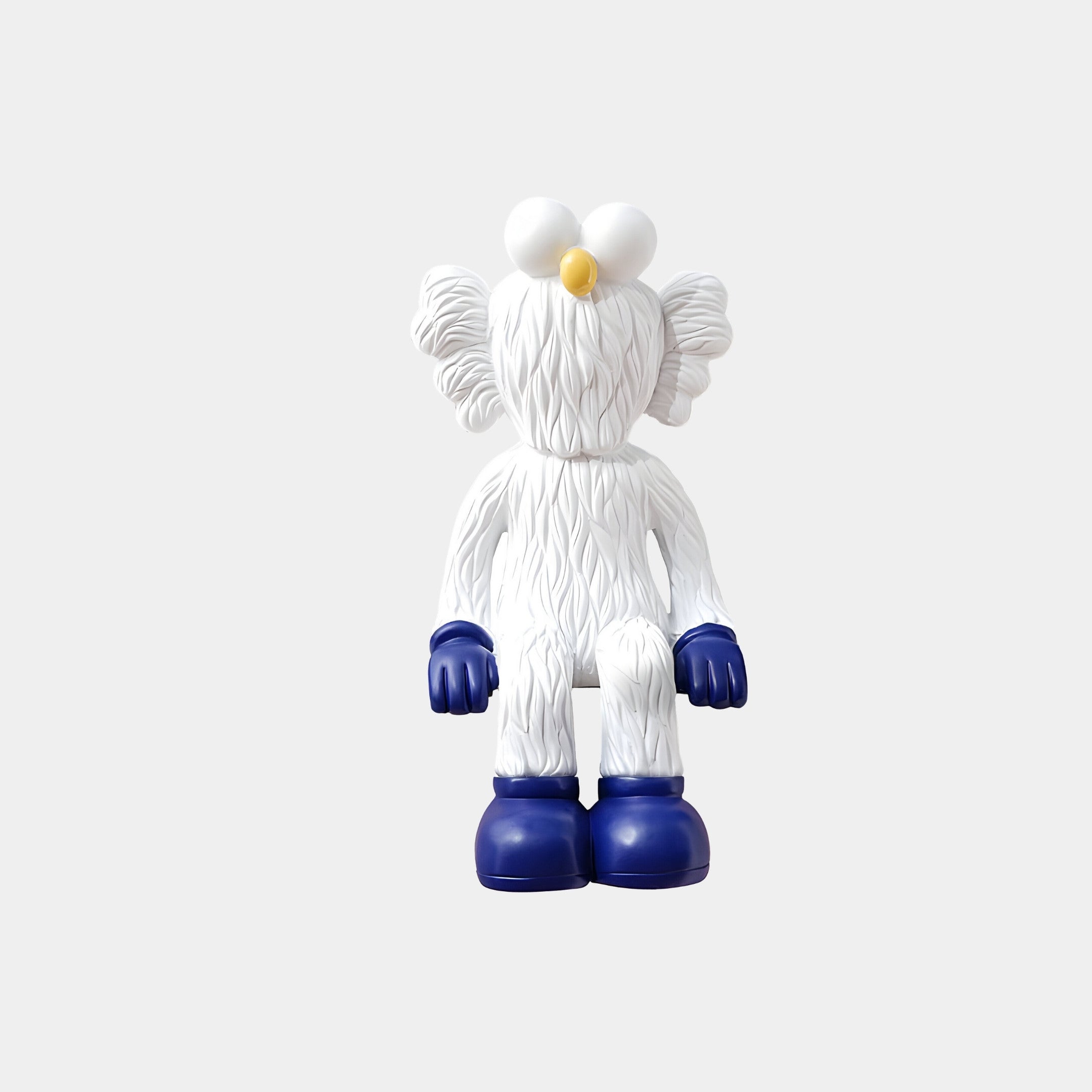 The White & Blue Iconify Furry Sitting Sculpture by Giant Sculptures is a 70cm masterpiece with large round eyes, a yellow nose, and fluffy ears. It features dark blue gloves and boots, ideal for contemporary interiors against a light gray background.