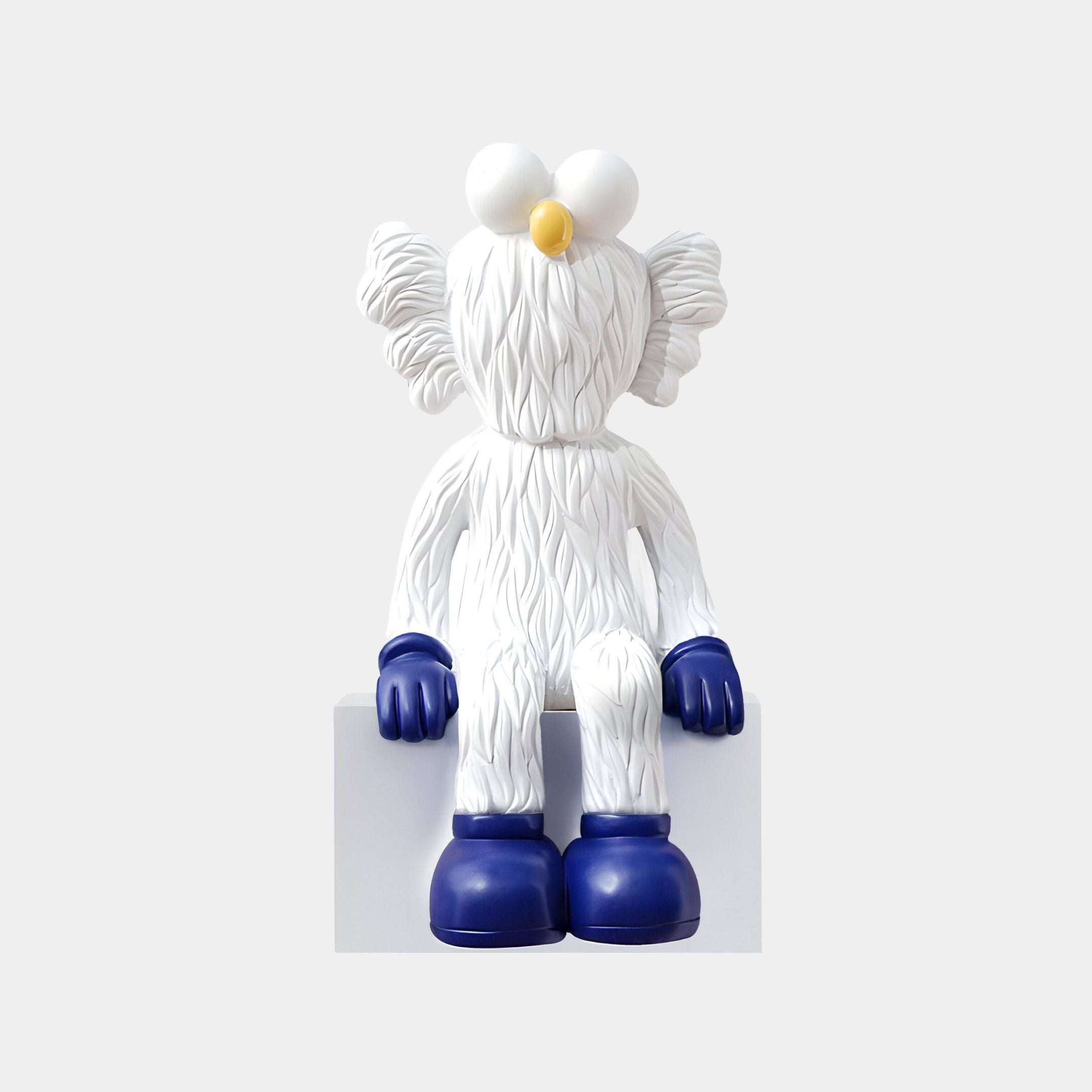 The Giant Sculptures White & Blue Iconify Furry Sitting Sculpture (70cm) features textured white fur, big round eyes, a yellow nose, and blue gloves and boots—ideal for adding modern charm to any contemporary space.