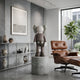 Hazelnut Brown Iconify Standing Sculpture, 70cm resin figure with mint-green ears and shorts, displayed on a concrete pedestal in a modern living room with an Eames lounge chair.