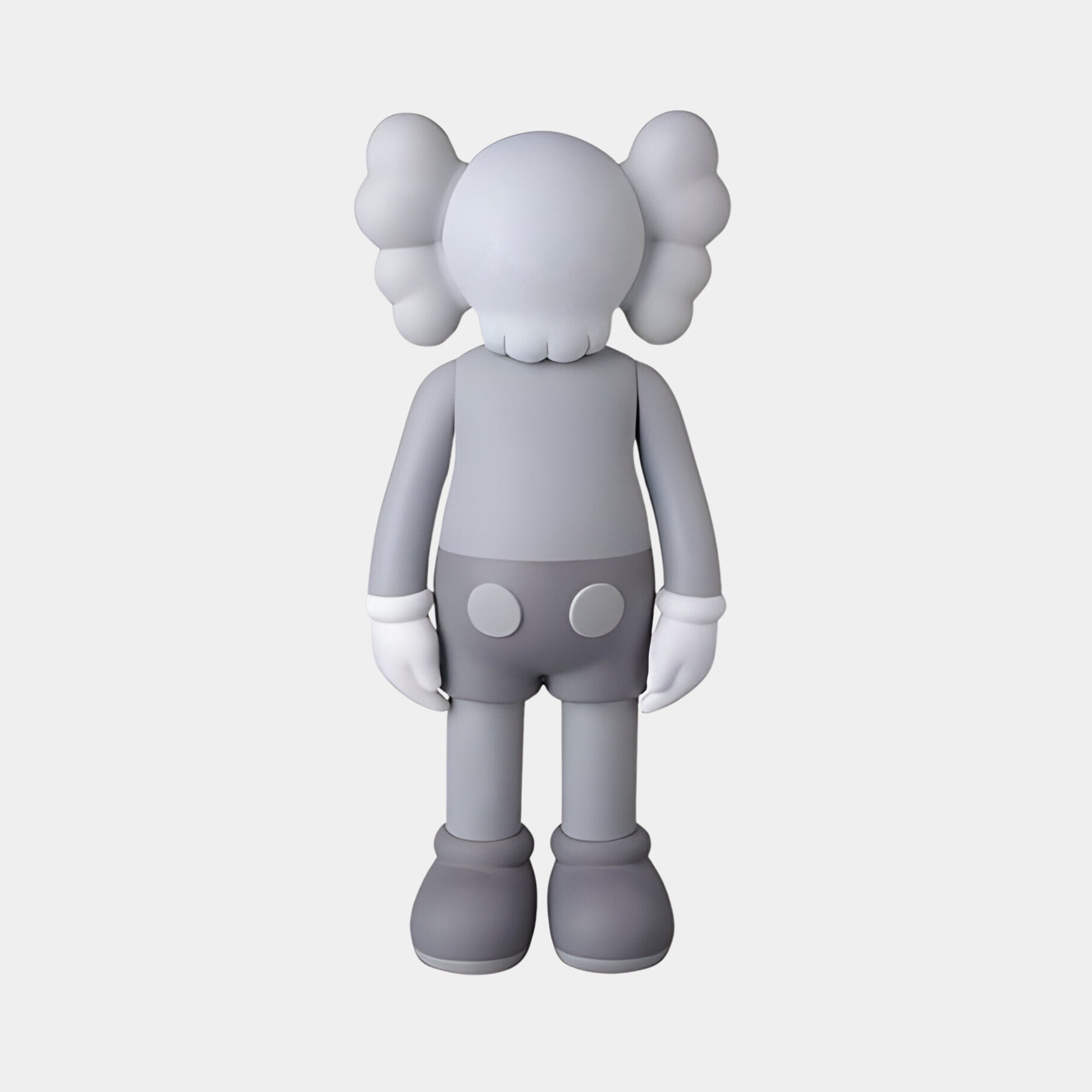 The Soft Grey Iconify Standing Sculpture by Giant Sculptures features a cartoon-like figure with oversized hands and feet, a featureless face, and bone/bow-like ears. It wears buttoned shorts and stands against a plain white background, ideal for enhancing contemporary interiors. Size: 70cm.