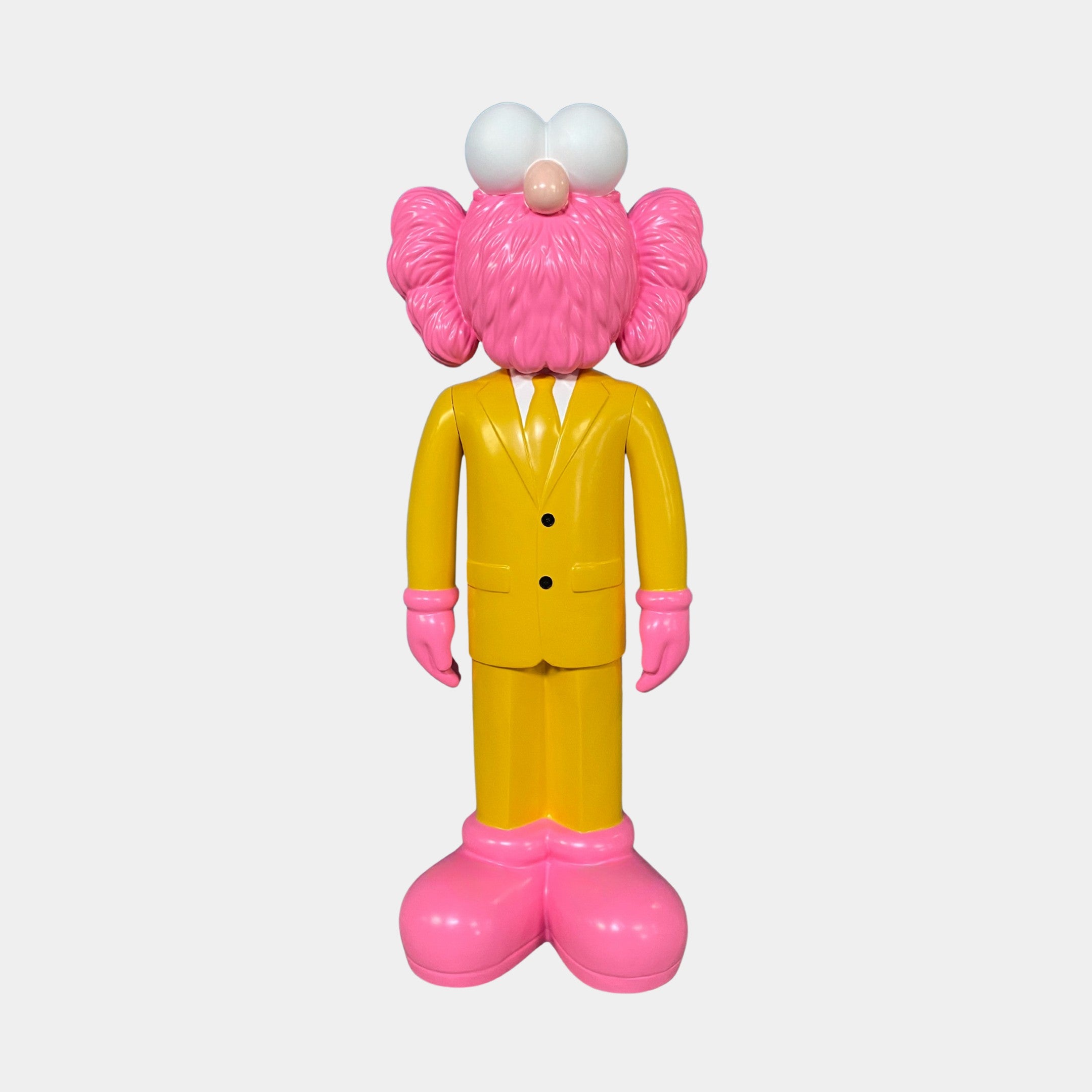The Giant Sculptures Sunbeam Yellow Suit Iconify CEO Sculpture (90cm) features a contemporary figurine with a pink, furry face, large white eyes, and pink hands and feet in a yellow suit—an ideal luxury decor piece for any modern workspace.