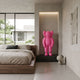 Electric Pink Iconify Rollo Sculpture, 80cm, displayed on a black platform in an alcove within a bedroom with a wooden bed frame.