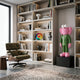 Forest Green Suit Iconify CEO Sculpture, 90cm, with pink fluffy head and pink shoes, displayed on a black plinth beside a bookshelf and green lounge chair.
