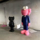 Deep Navy Blue Suit Iconify CEO Sculpture 200cm by Giant Sculptures, shown beside a smaller black Iconify figure against a textured grey brick wall.