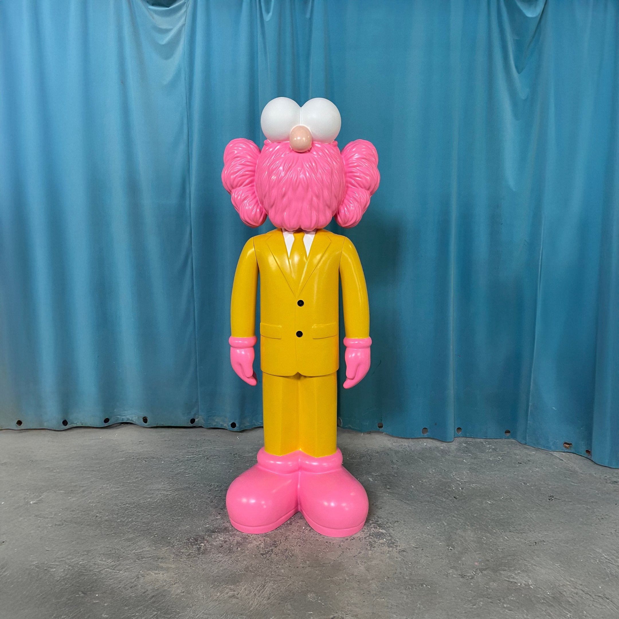 The Sunbeam Yellow Suit Iconify CEO Sculpture by Giant Sculptures stands 90cm tall with oversized pink features and cartoonish white eyes, making it a playful contemporary resin piece or luxury workspace decor.
