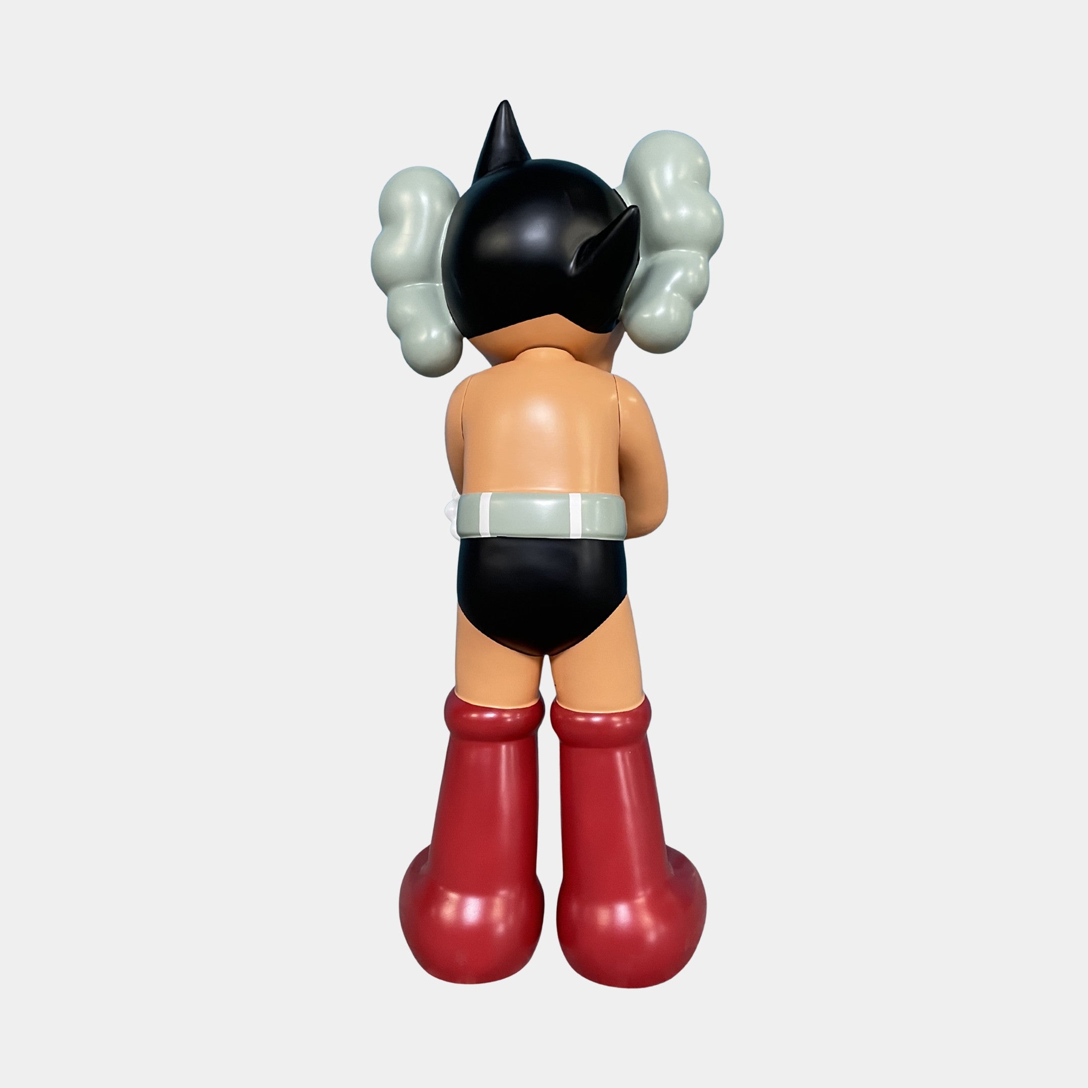 The Fiery Red Iconify Cosmic Boy Sculpture - 140cm by Giant Sculptures features black spiky hair, gray side puffs, black briefs, a white belt, and tall red boots, shown from behind against a plain background.