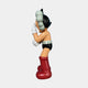 A side view of the Fiery Red Iconify Cosmic Boy Sculpture by Giant Sculptures shows a colorful, cartoon-like resin figure (140cm) in red boots, black shorts, white gloves, and a black helmet, with one hand covering its face against a plain white background.