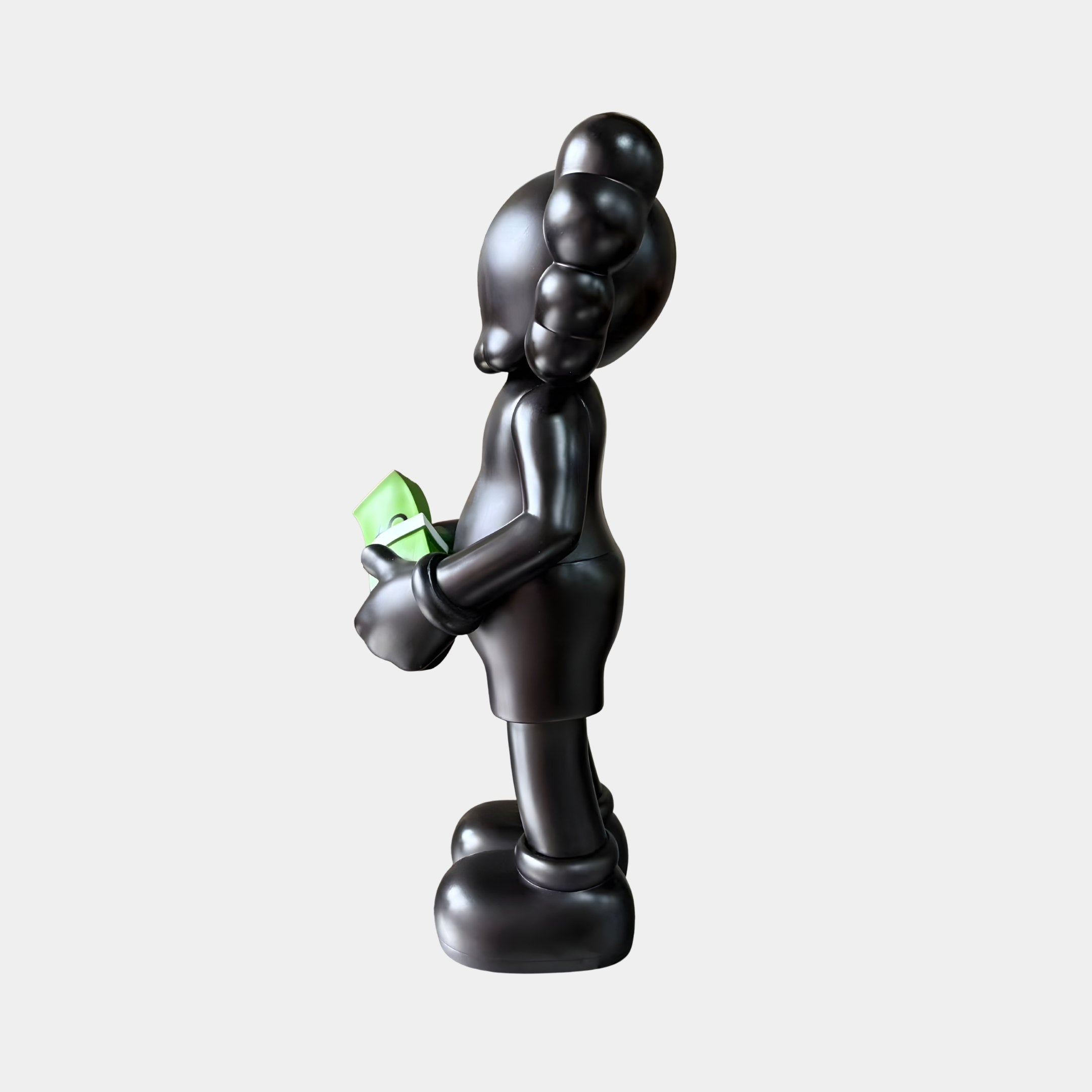 Side view of the Midnight Black Iconify Dollars Figure (30cm) by Giant Sculptures in matte black polyvinyl, holding a green dollar stack, on a plain background.