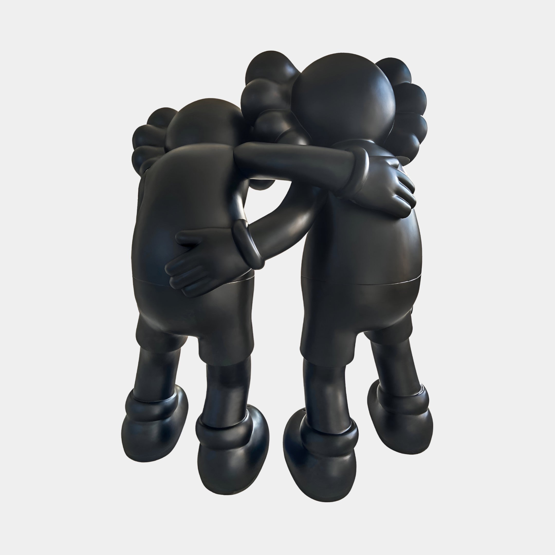 Two black cartoon-like figures stand in a warm embrace. The Midnight Black Iconify Friendship Sculpture - 150cm by Giant Sculptures is perfect for modern resin sculpture collections or contemporary art displays.