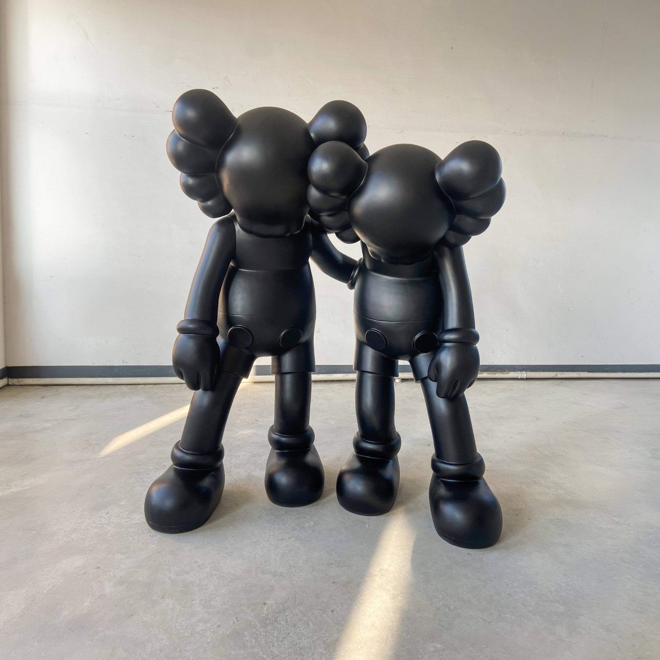 The Midnight Black Iconify Friendship Sculpture - 150cm by Giant Sculptures features two large, matte black figures side by side, one resting its hand on the other's shoulder—a striking contemporary symbol of comfort and companionship.