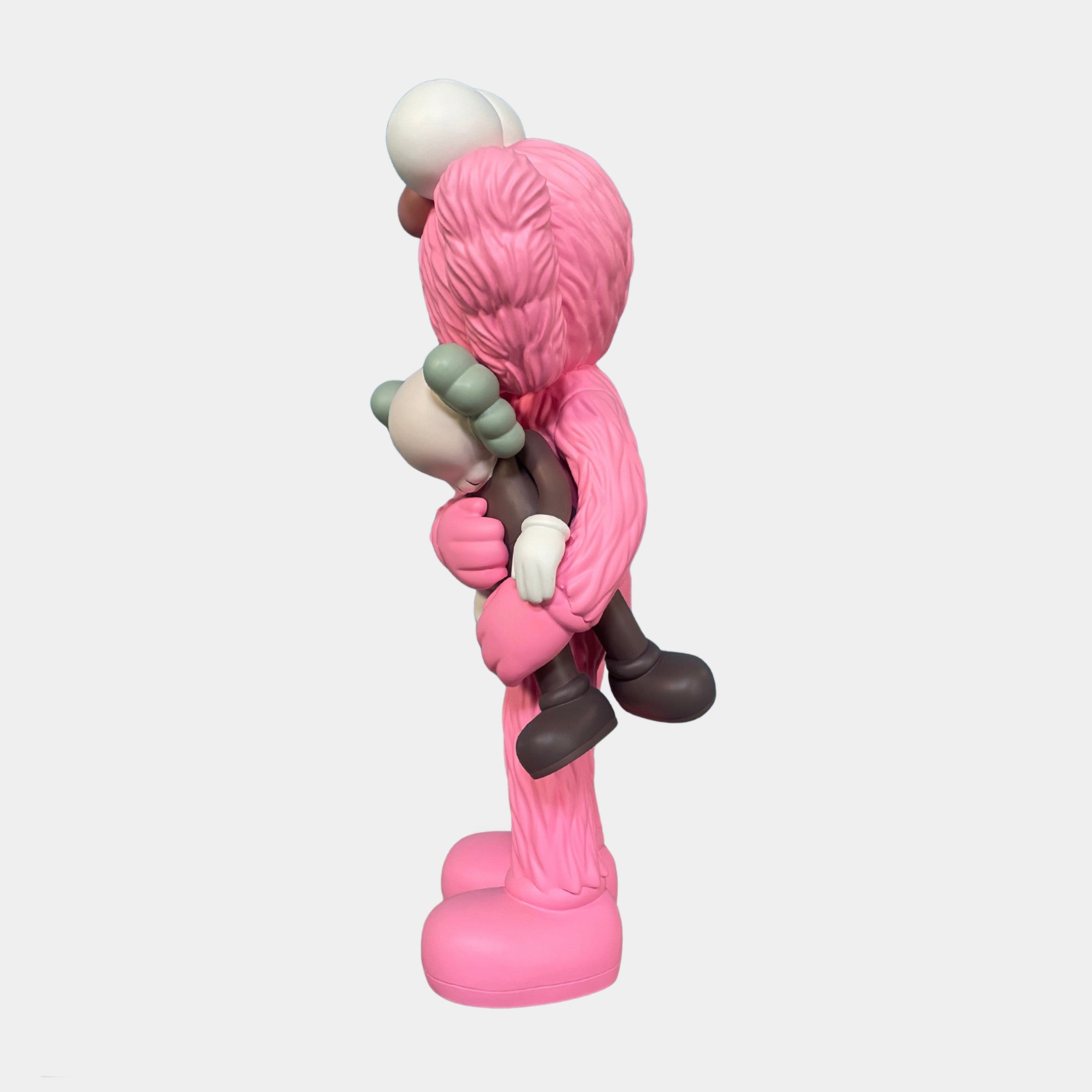 The Giant Sculptures Petal Pink Iconify Loving Furry Sculpture (135cm) features a pink, furry cartoon figure with crossed-out eyes holding a smaller gray and white character—an artistic home decor piece against a white background.