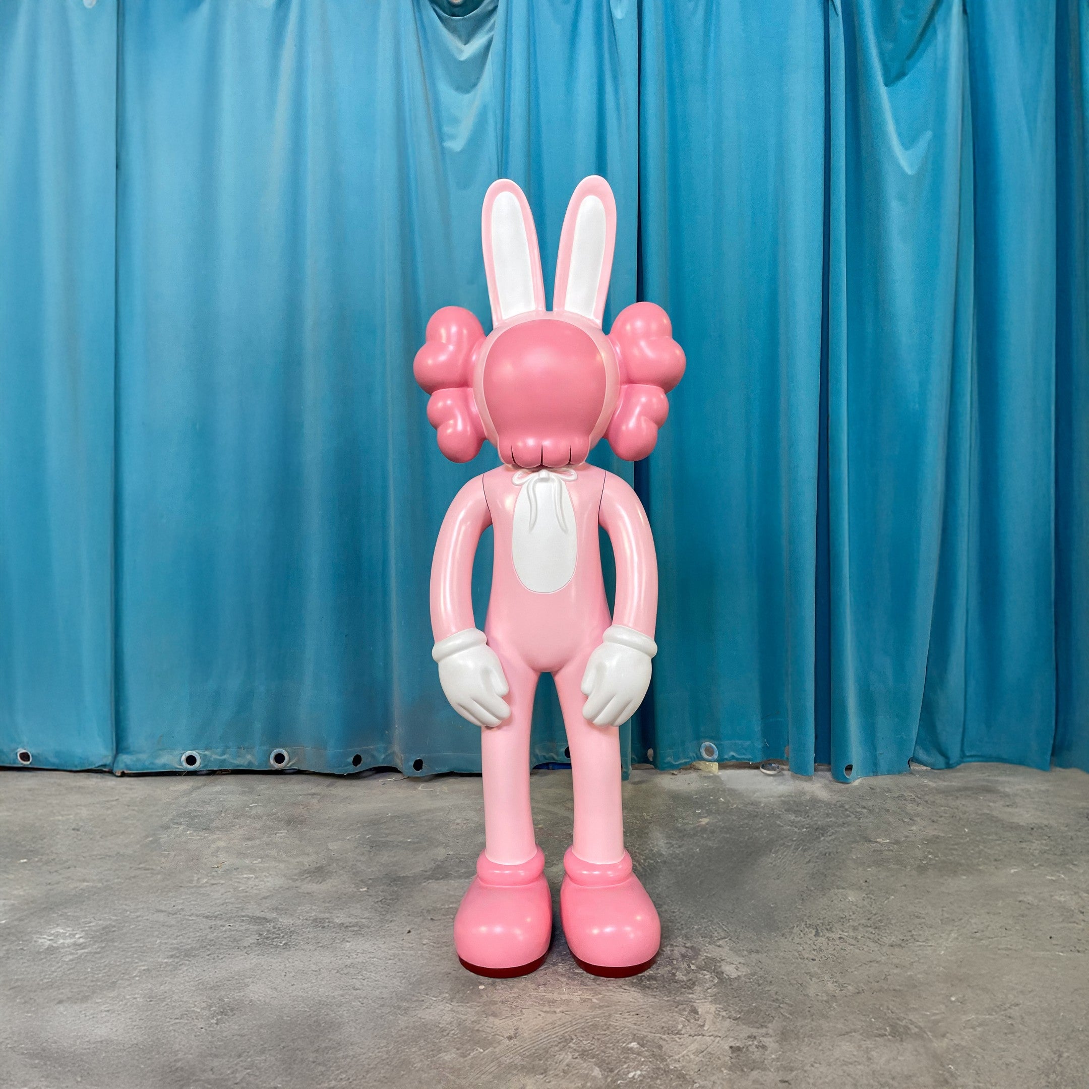 The Coral Pink Iconify Rabbit Sculpture - 130cm by Giant Sculptures features a large pink and white cartoon rabbit with X-shaped eyes, big ears, gloved hands, and downturned arms—perfect as bold coral pink decor.