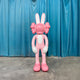 The Coral Pink Iconify Rabbit Sculpture - 130cm by Giant Sculptures features a large pink and white cartoon rabbit with X-shaped eyes, big ears, gloved hands, and downturned arms—perfect as bold coral pink decor.