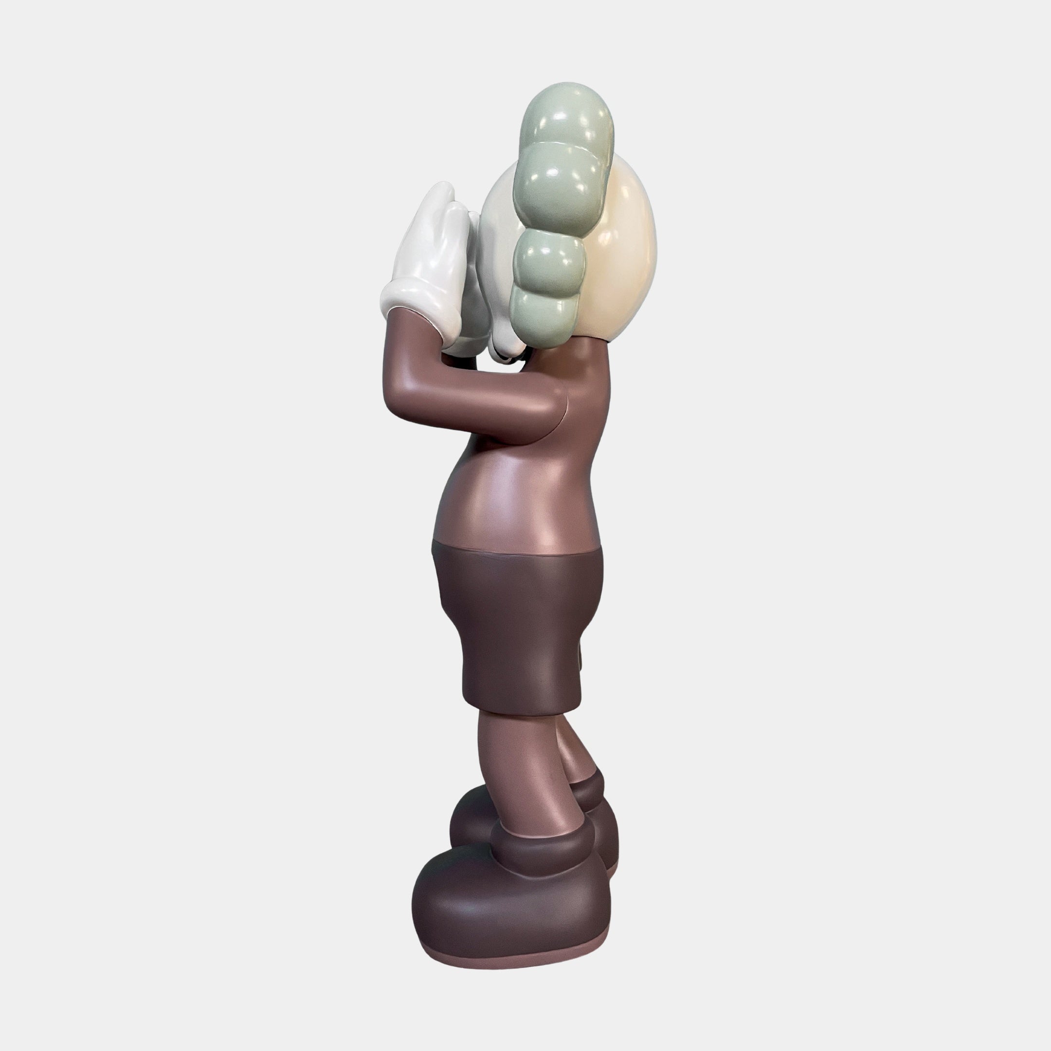 Side view of the Hazelnut Brown Iconify Silent Cry Sculpture - 91cm by Giant Sculptures, featuring X-ed out eyes, gray gloved hands covering its face, black shorts, and light green hair. Ideal contemporary art decor on a plain white background.