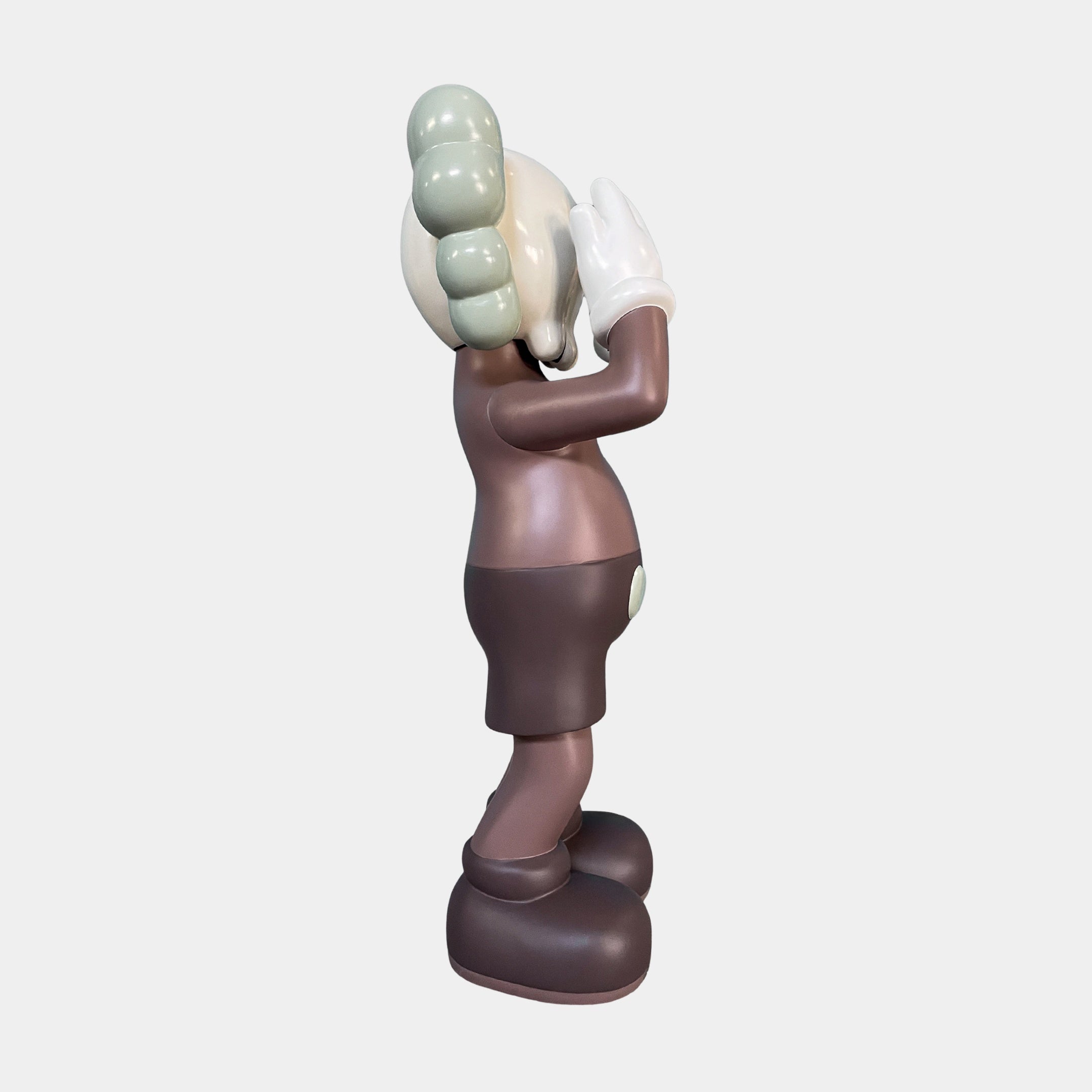 Side view of the Hazelnut Brown Iconify Silent Cry Sculpture (91cm) by Giant Sculptures, featuring a stylized cartoon figure in muted brown and green with gloved hands over its face—an ideal piece for contemporary art decor.