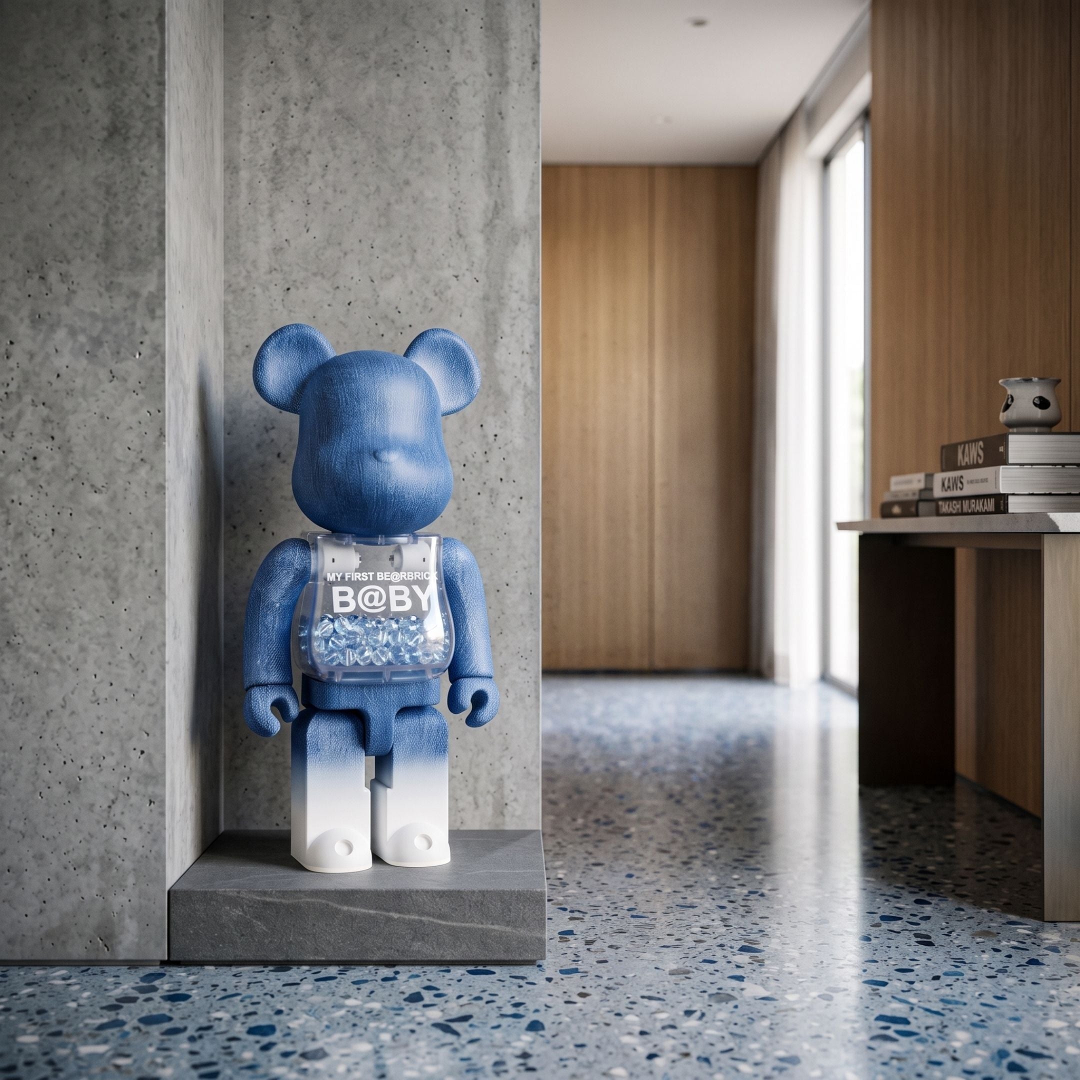 Indigo Fade Bear Sculpture, 70cm, in blue denim-print resin finish with transparent "BABY" chest cavity, displayed on a stone ledge in a modern hallway.