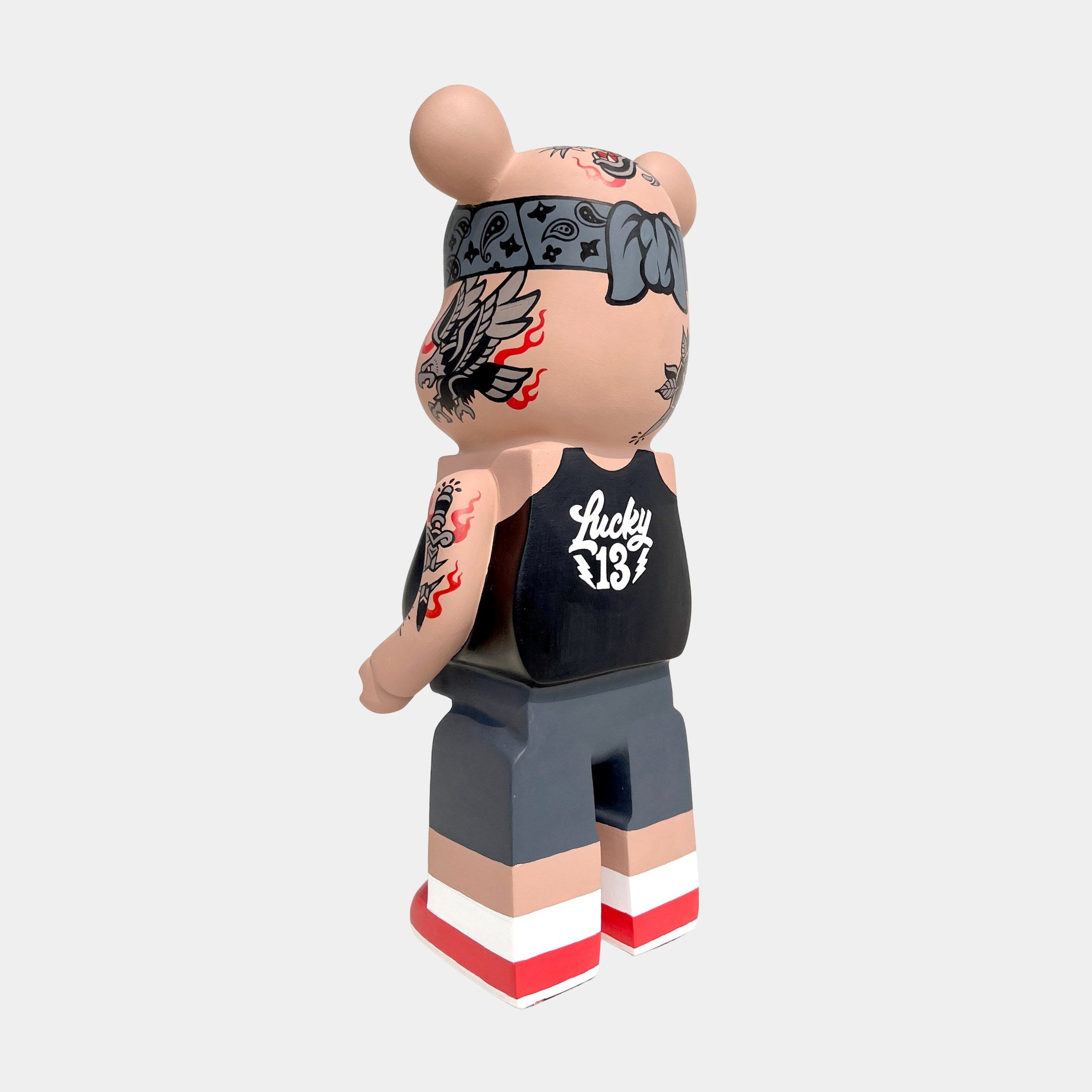 The Iron Paw Bear Sculpture - 135cm by Giant Sculptures is a limited edition vinyl bear figurine featuring tattoos, a bandana, black Lucky 13 tank top, gray shorts, and red-and-white striped shoes, shown from behind on a plain background.