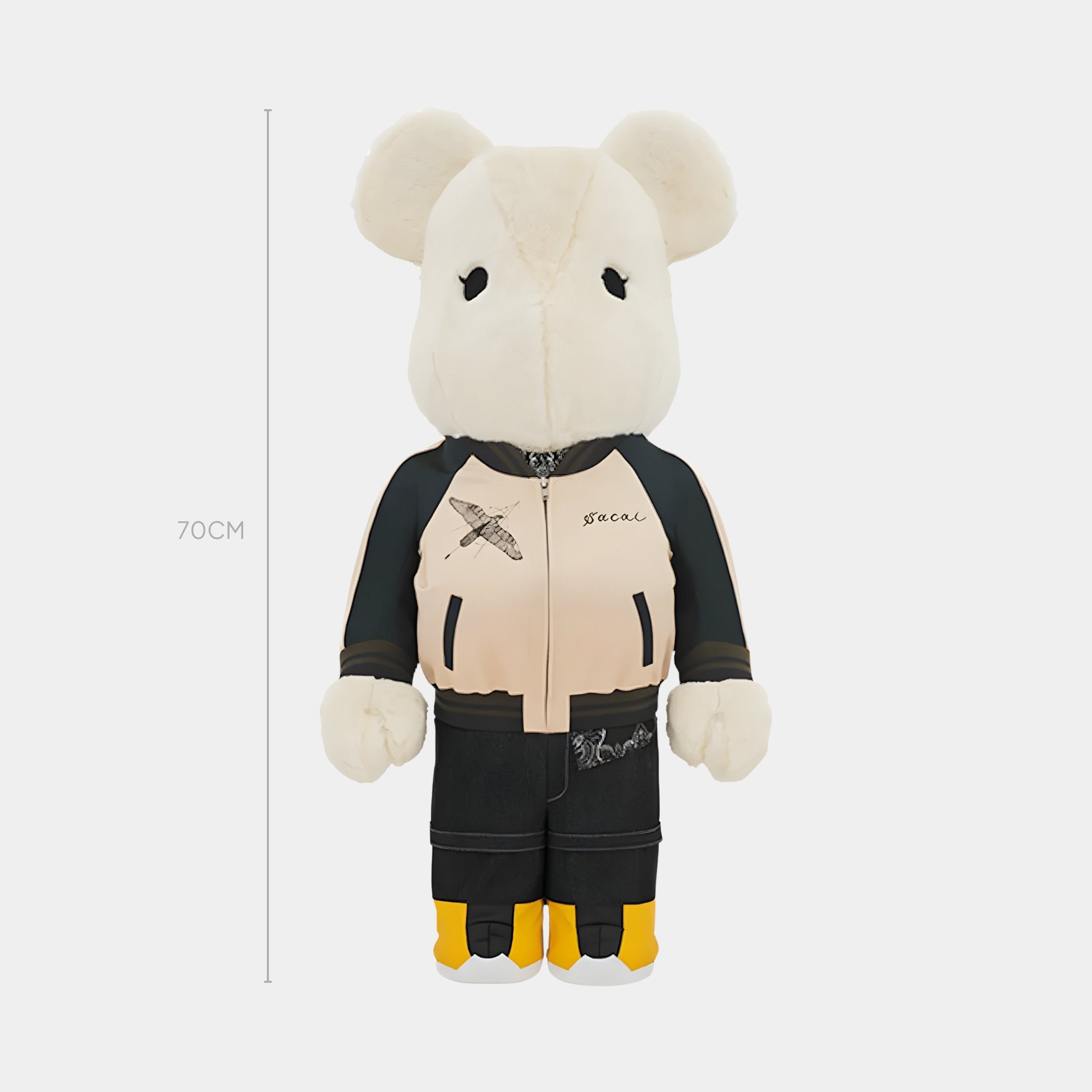 The Jacket Clad Plush Bear Sculpture by Giant Sculptures stands 70cm tall with a cream head and hands, black eyes, streetwear-style beige and black jacket, dark pants, yellow socks, and is set against a plain white background.