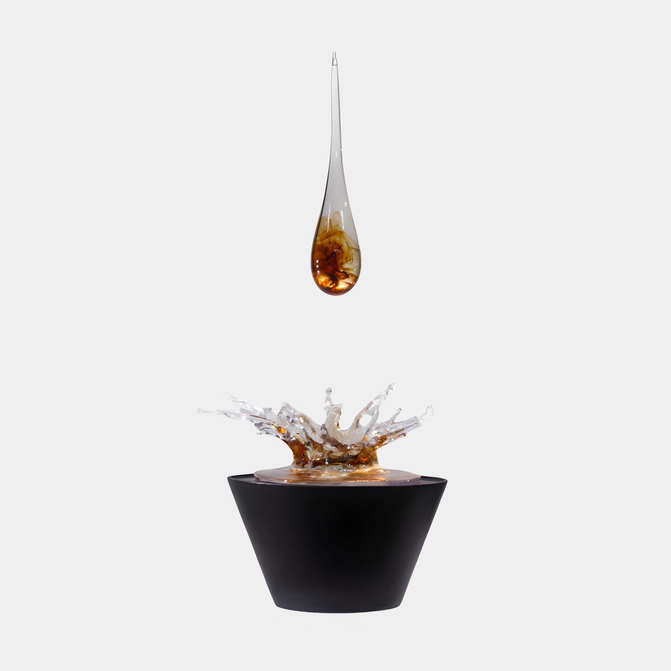 Amber Resin Water Splash Teardrop on Black Basin Sculpture by Giant Sculptures, suspended droplet above a clear splash crown on a black basin, plain background.